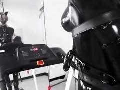 Restrained girl in black latex outfit walks on treadmill